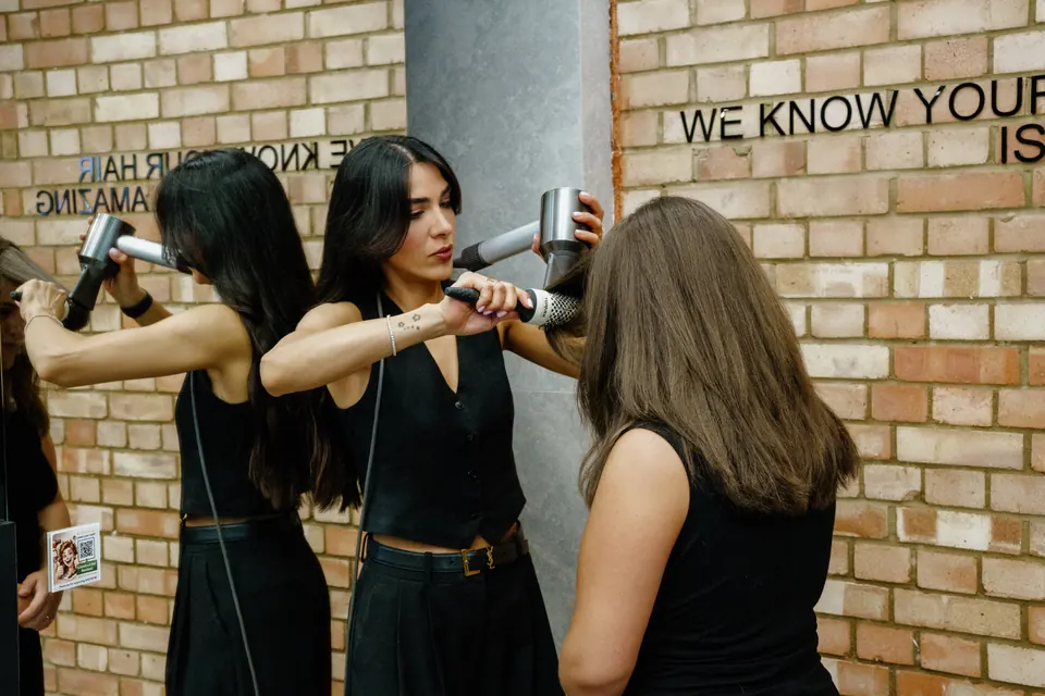 Two stylists blow-drying at the brick wall