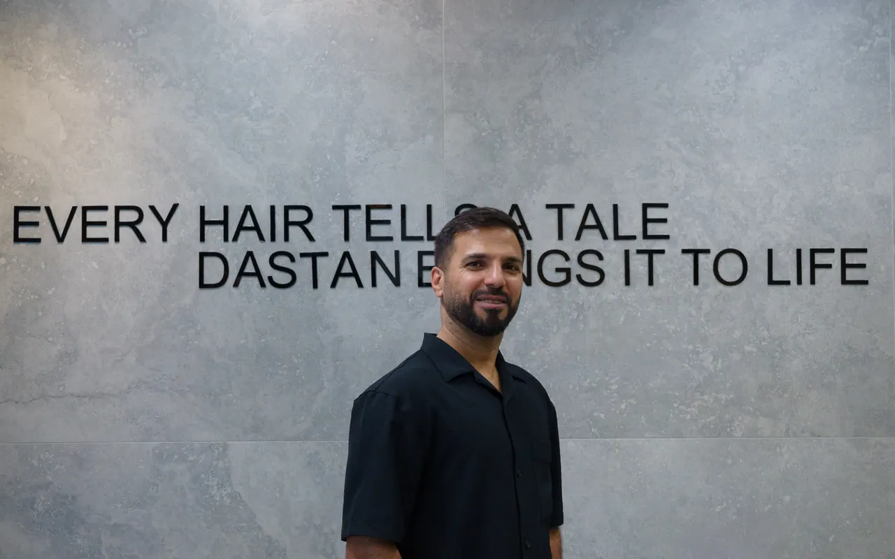 Sam in front of the concrete wall that reads “Every hair tells a tale, Dastan brings it to life”