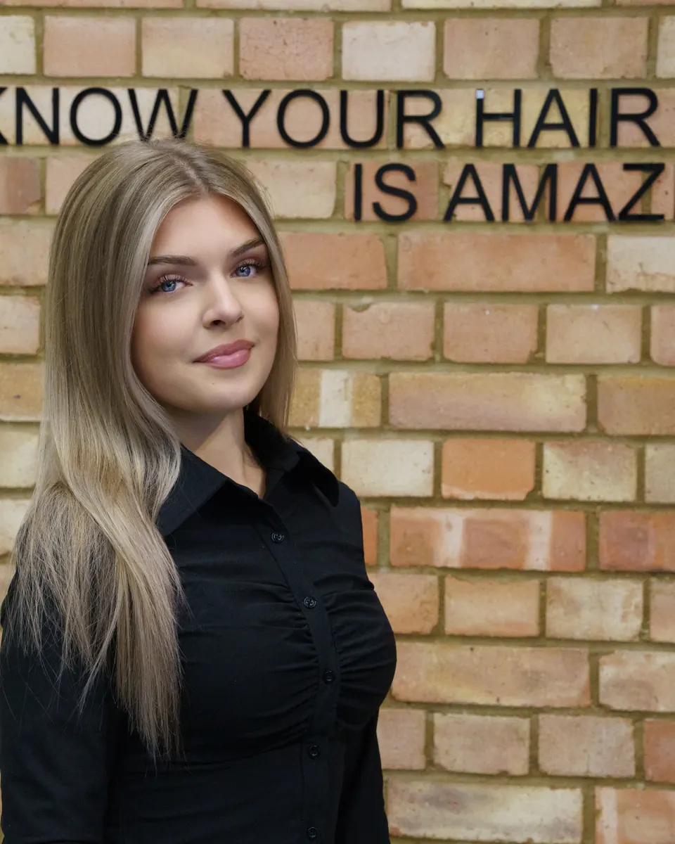 A client with long, glossy blonde hair in front of the brick wall