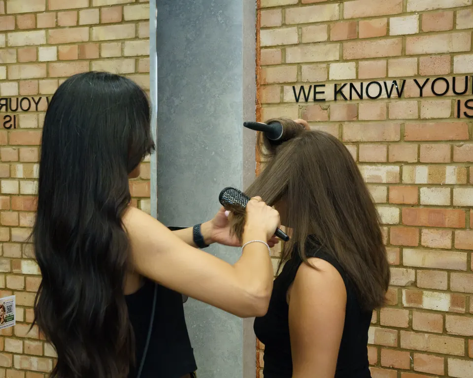 Fatima styling a client’s long dark hair with a round brush