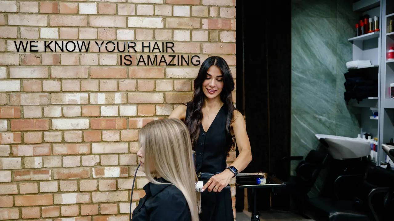 Fatima with a client by the brick wall that reads “We know your hair is amazing”